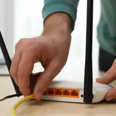 Ręka podłącza żółty kabel do routera, co może pomóc w rozwiązaniu problemu, jak wzmocnić sygnał wifi w domu.