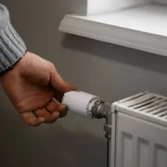 Dłoń reguluje termostat grzejnika, by zapewnić optymalną temperaturę w pomieszczeniu.
