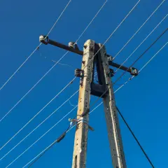 Betonowy słup energetyczny z przewodami na tle błękitnego nieba.