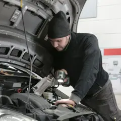 Mechanik z latarką bada silnik Renault, szukając przyczyny błędu DTC P0380.