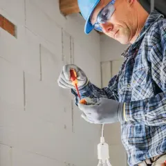 Elektryk w kasku i okularach montuje oprawkę żarówki, tworząc punkt elektryczny.