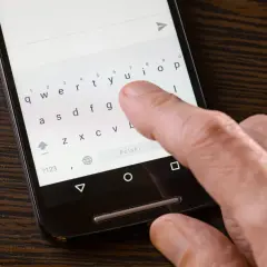 Dłoń pisze na smartfonie, klawiatura pokazuje brak polskich znaków w sms.