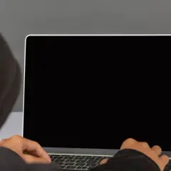 Osoba w kapturze pisze na laptopie. Dowiedz się, jak podłączyć monitor do laptopa, aby rozszerzyć przestrzeń roboczą.