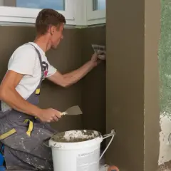 Remont starego domu: fachowiec tynkuje ścianę, pokazując, jak wyrównać ściany w starym domu.