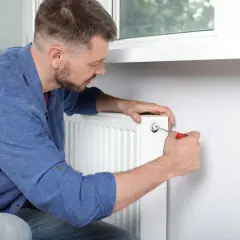Mężczyzna używa śrubokręta, by odpowietrzyć grzejniki. To prosty sposób na pozbycie się powietrza z instalacji grzewczej.