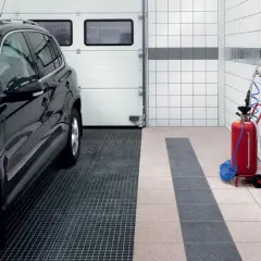 Nowoczesna wylewka pod garaż z kratką odpływową, obok czarny SUV i czerwony dystrybutor płynów.