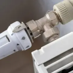 Wymiana termostatu w grzejniku bez spuszczania wody. Biała głowica termostatu z oznaczeniami temperatury przykręcona do zaworu grzejnikowego.
