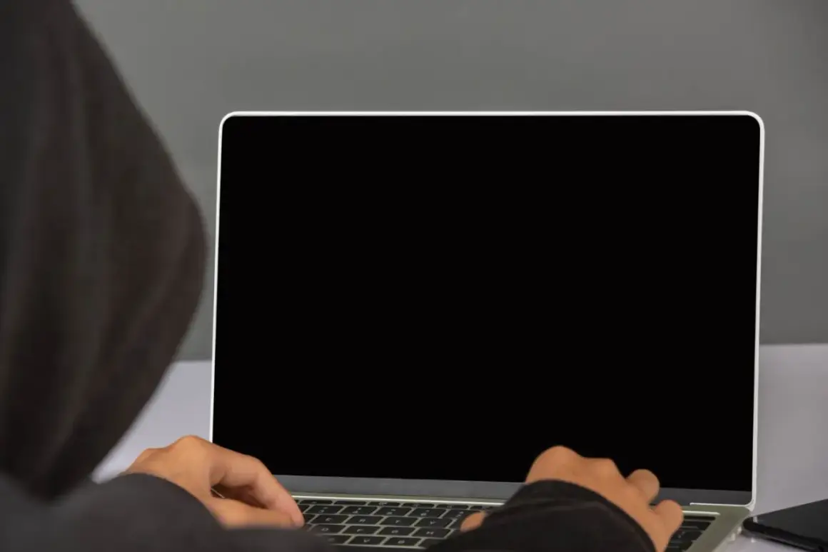 Osoba w kapturze pisze na laptopie. Dowiedz się, jak podłączyć monitor do laptopa, aby rozszerzyć przestrzeń roboczą.