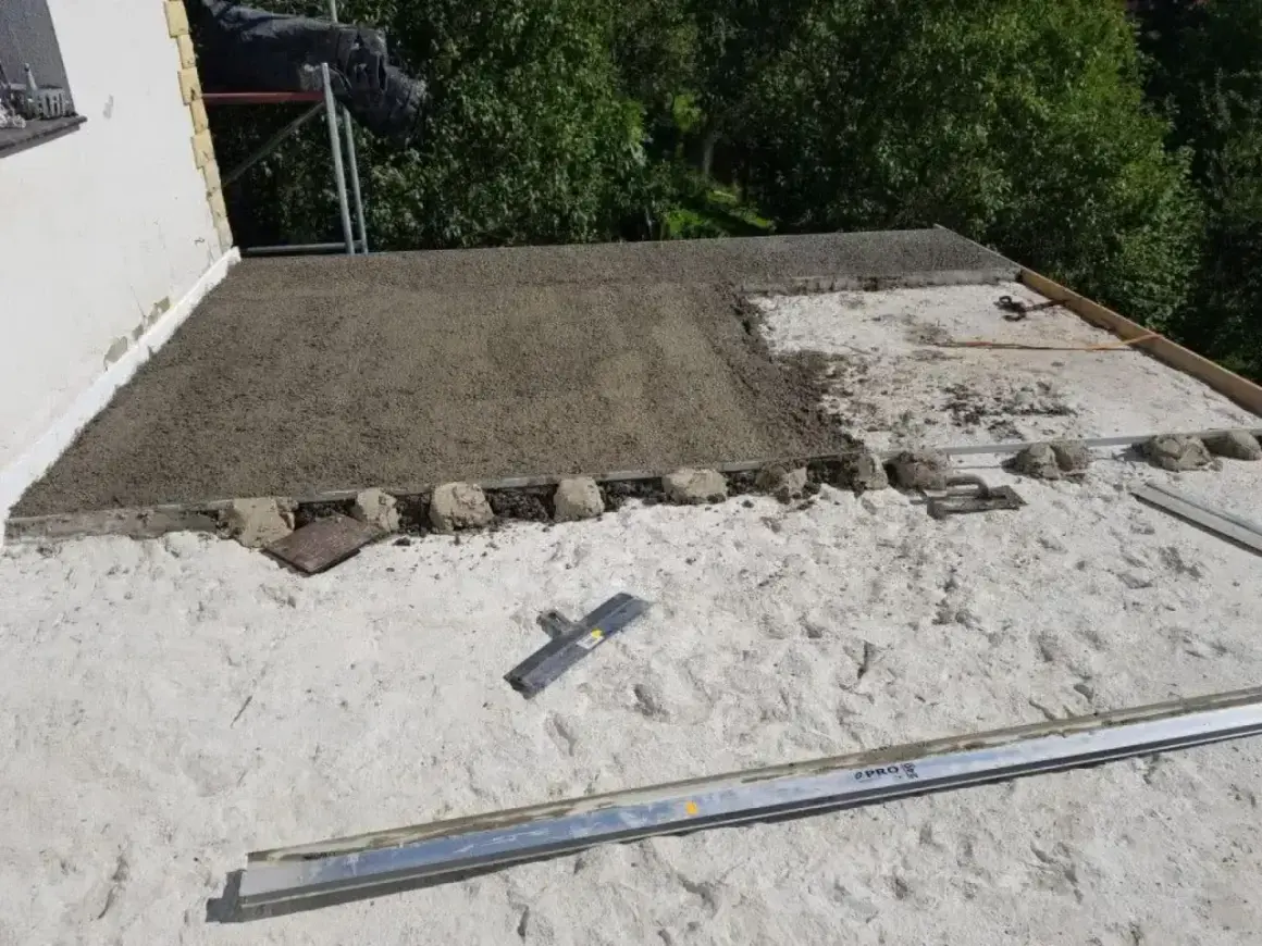 Budowa dachu z wykorzystaniem styrobetonu. Widać świeżo wylany materiał, który czeka na dalsze prace. Kluczowe są odpowiednie proporcje styrobetonu.