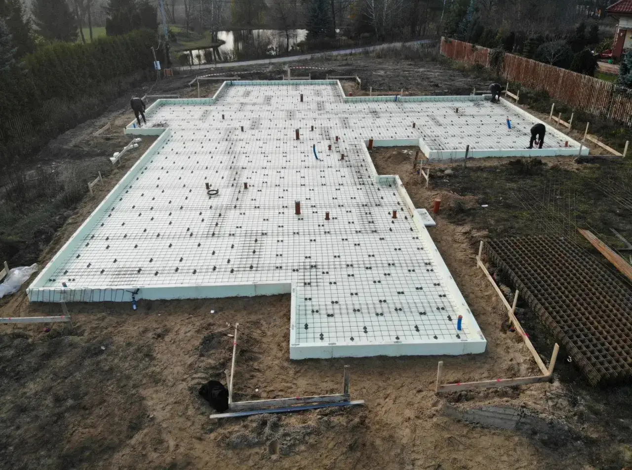 Budowa wylewki pod garaż. Na placu budowy widać fundamenty z izolacją, zbrojenie i rury.