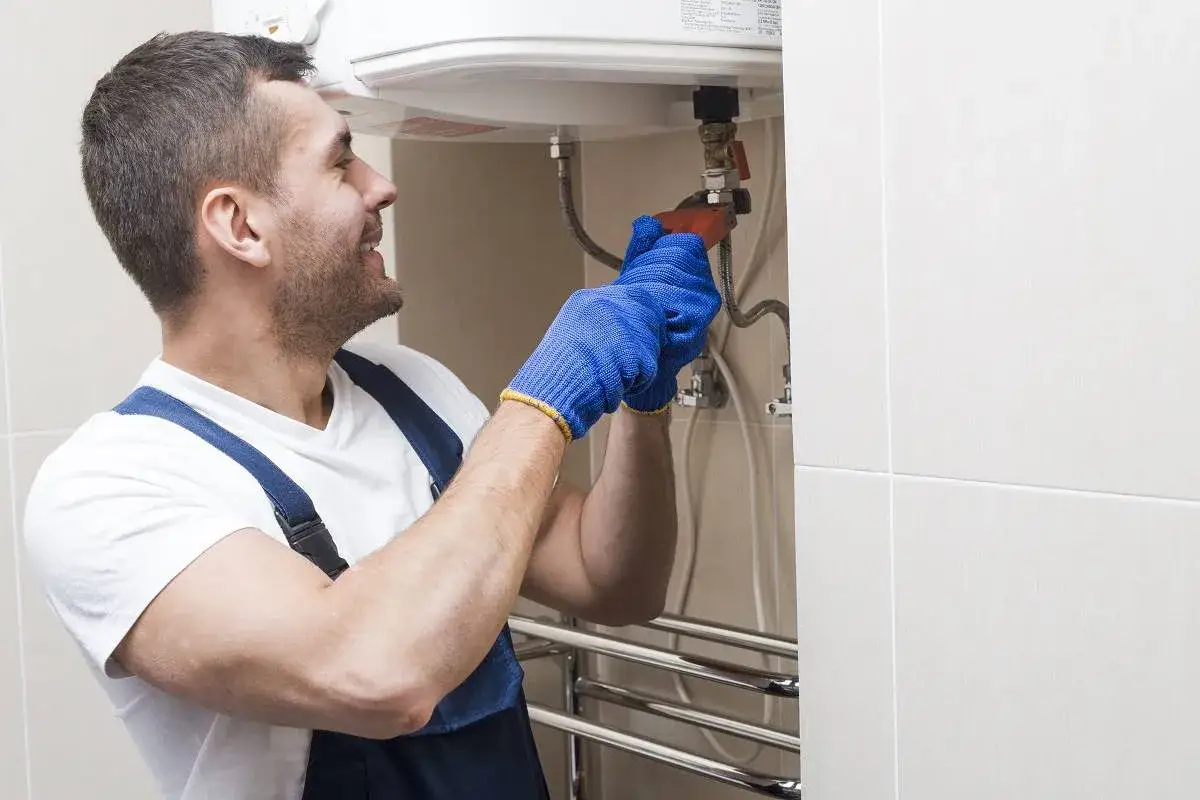 Instalator w niebieskich rękawiczkach dokręca zawór, pokazując, jak spuścić wodę z bojlera.