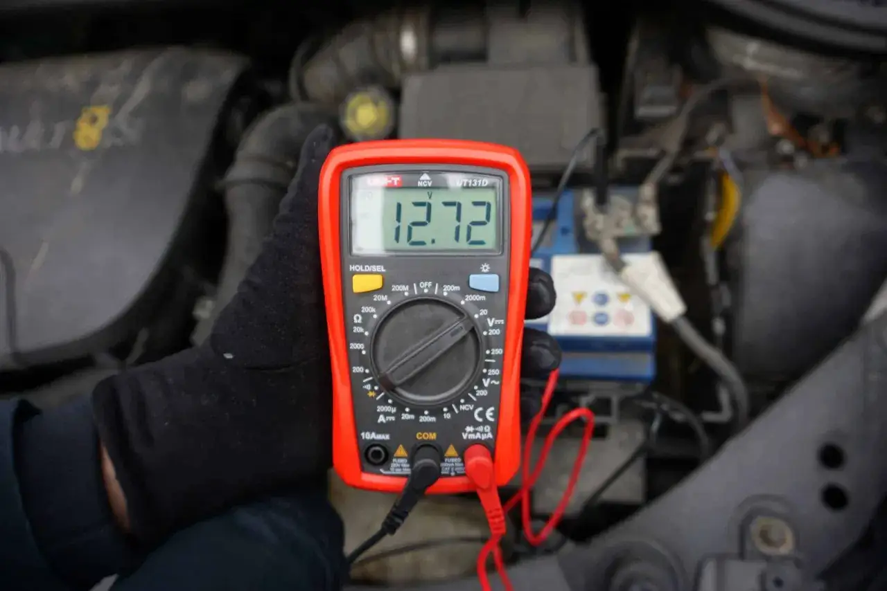 Pomiar napięcia akumulatora multimetrem pokazuje 12.72V.
