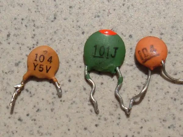Trzy ceramiczne kondensatory z widocznymi oznaczeniami, np. "104".