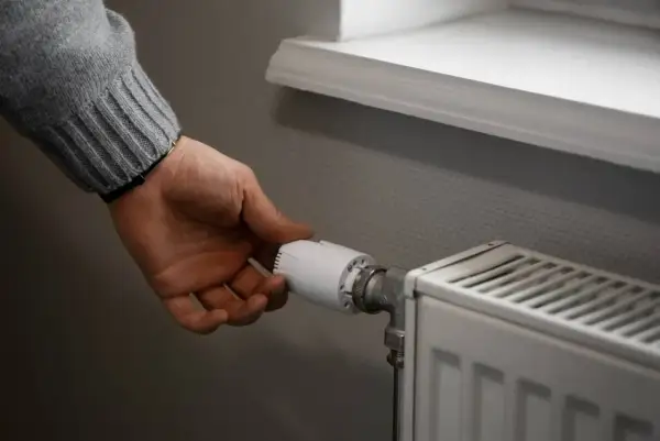 Dłoń reguluje termostat grzejnika, by zapewnić optymalną temperaturę w pomieszczeniu.