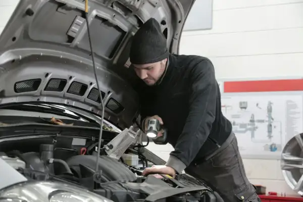 Mechanik z latarką bada silnik Renault, szukając przyczyny błędu DTC P0380.