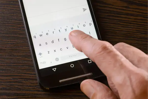 Dłoń pisze na smartfonie, klawiatura pokazuje brak polskich znaków w sms.
