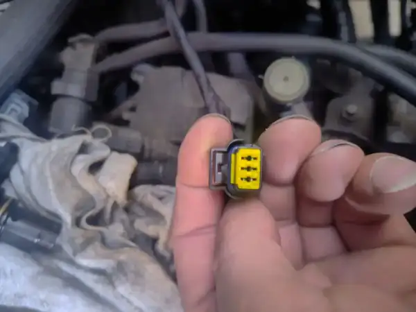 Wtyczka z żółtym wkładem, być może związana z błędem **dtc p1693 volkswagen**. W tle widać fragmenty silnika.
