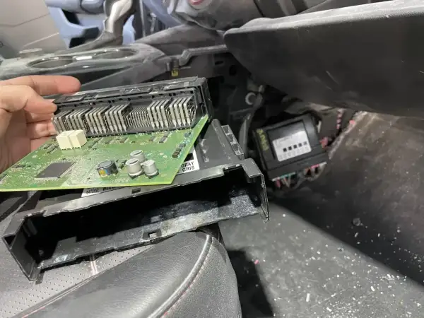 Ręka trzyma moduł elektroniczny z zieloną płytką drukowaną, prawdopodobnie związany z błędem dtc u0140 opel. Obok widoczny inny moduł.