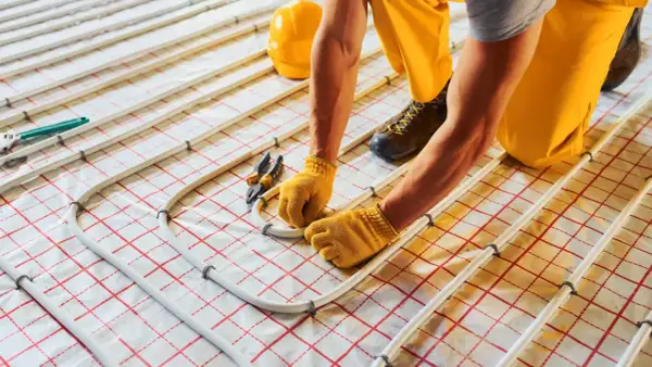 Instalator montuje rury do suchego ogrzewania podłogowego. Wady tego systemu mogą obejmować nierównomierne grzanie.